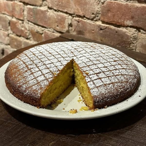 A round cake with a slice removed, dusted with powdered sugar in a diamond pattern.