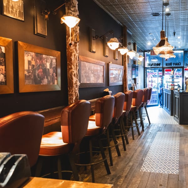 Interior of Brooklyn DOP, a pizza restaurant, with a row of bar stools and framed pictures.