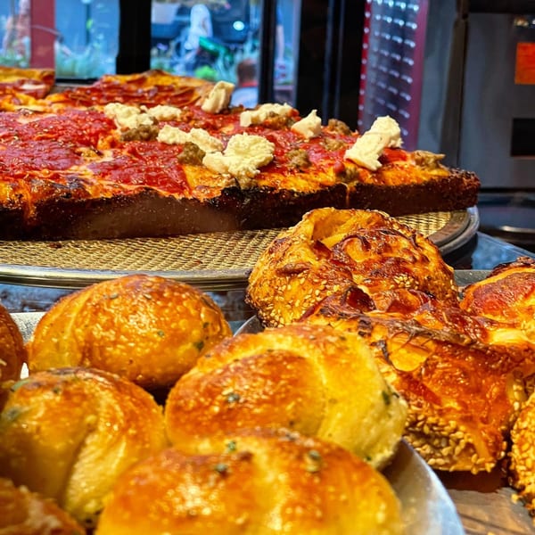 Close-up of Brooklyn DOP's square pizza with sausage and ricotta, alongside golden baked bread.