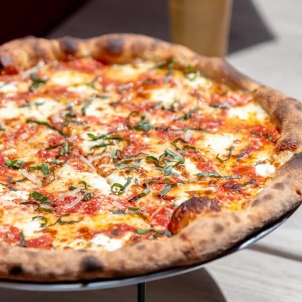 Close-up of a Brooklyn DOP pizza with melted cheese, red sauce, and fresh basil on a stand.