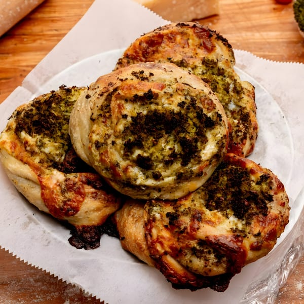 A plate of five golden-brown Brooklyn DOP pesto and cheese pinwheels on white parchment paper.