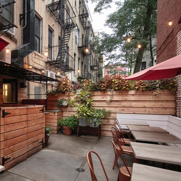 Outdoor dining patio with wooden planters, string lights, and tables with metal chairs.