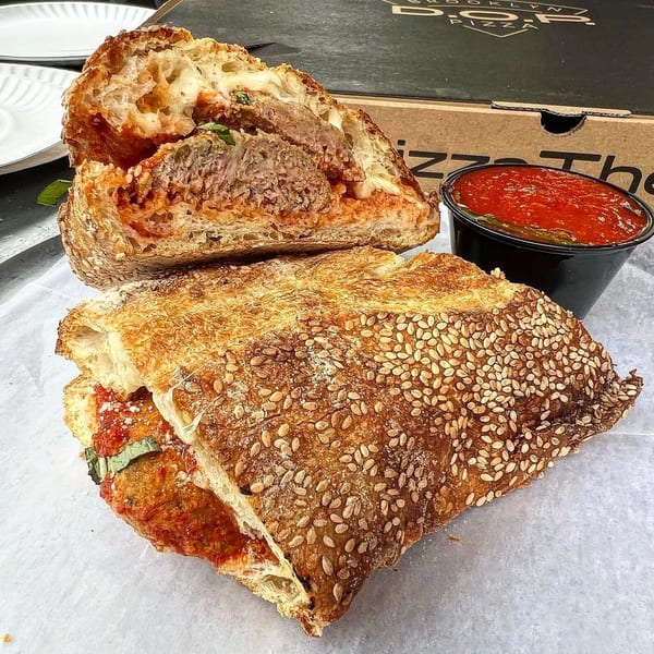 Meatball hero sandwich, cut in half, with a side of marinara sauce and a Brooklyn DOP pizza box.