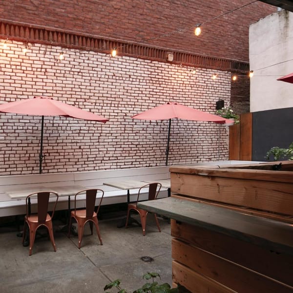 Outdoor patio at Brooklyn DOP with brick walls, string lights, orange umbrellas, and wooden seating.