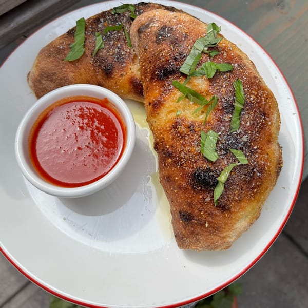 Two golden-brown calzones, topped with basil and salt, served with a side of red sauce.