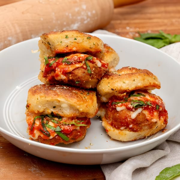 Four Brooklyn DOP meatball sliders with melted cheese, marinara, and basil on a white plate.