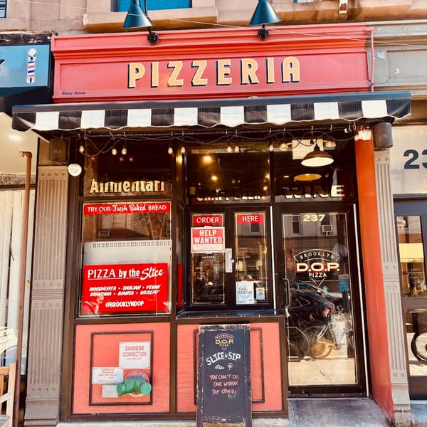 The red and black storefront of Brooklyn D.O.P. Pizzeria, with a "Pizzeria" sign and a chalkboard.