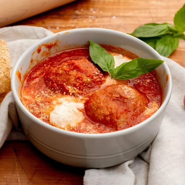 Meatballs in marinara sauce with ricotta and basil, served in a white bowl.